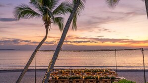 Un espace de restauration aménagé sur la plage, avec des tables, des chaises et des guirlandes lumineuses, offrant une vue sur l’océan.