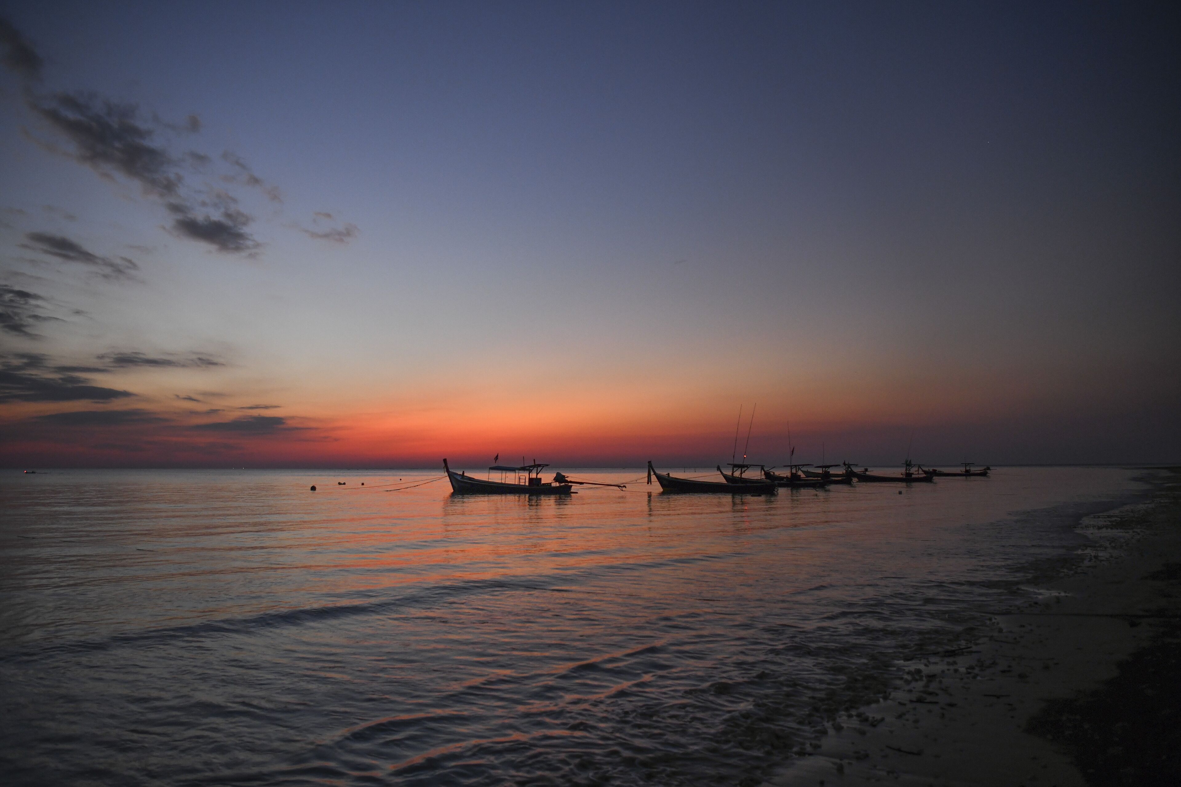 Ein ruhiges Meer bei Sonnenuntergang, mit mehreren vor Anker liegenden Booten.