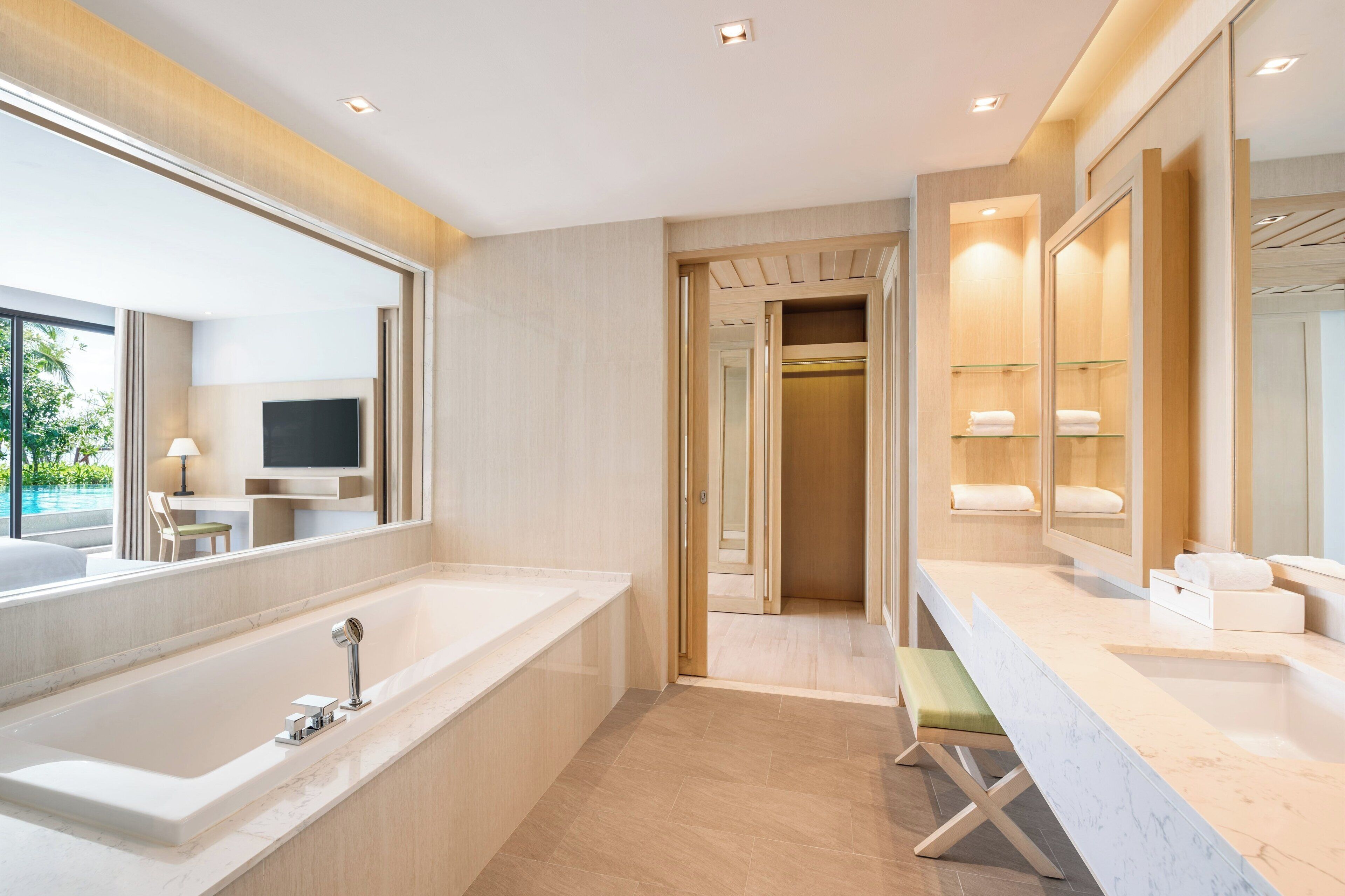A modern bathroom with a large bathtub, a vanity with a mirror, and a walk-in closet.