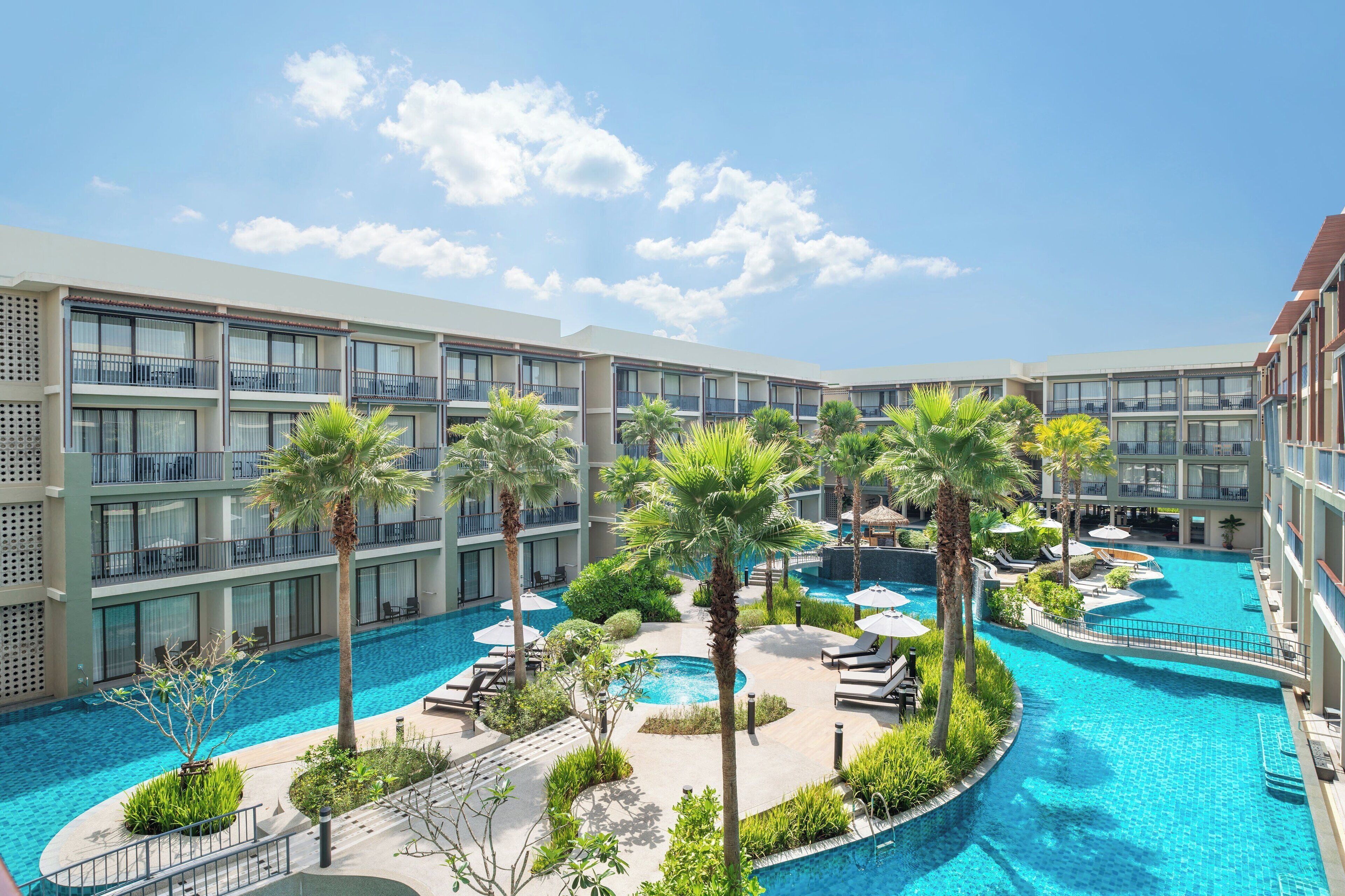 Un hotel con piscina central rodeada de palmeras y sillas de descanso.