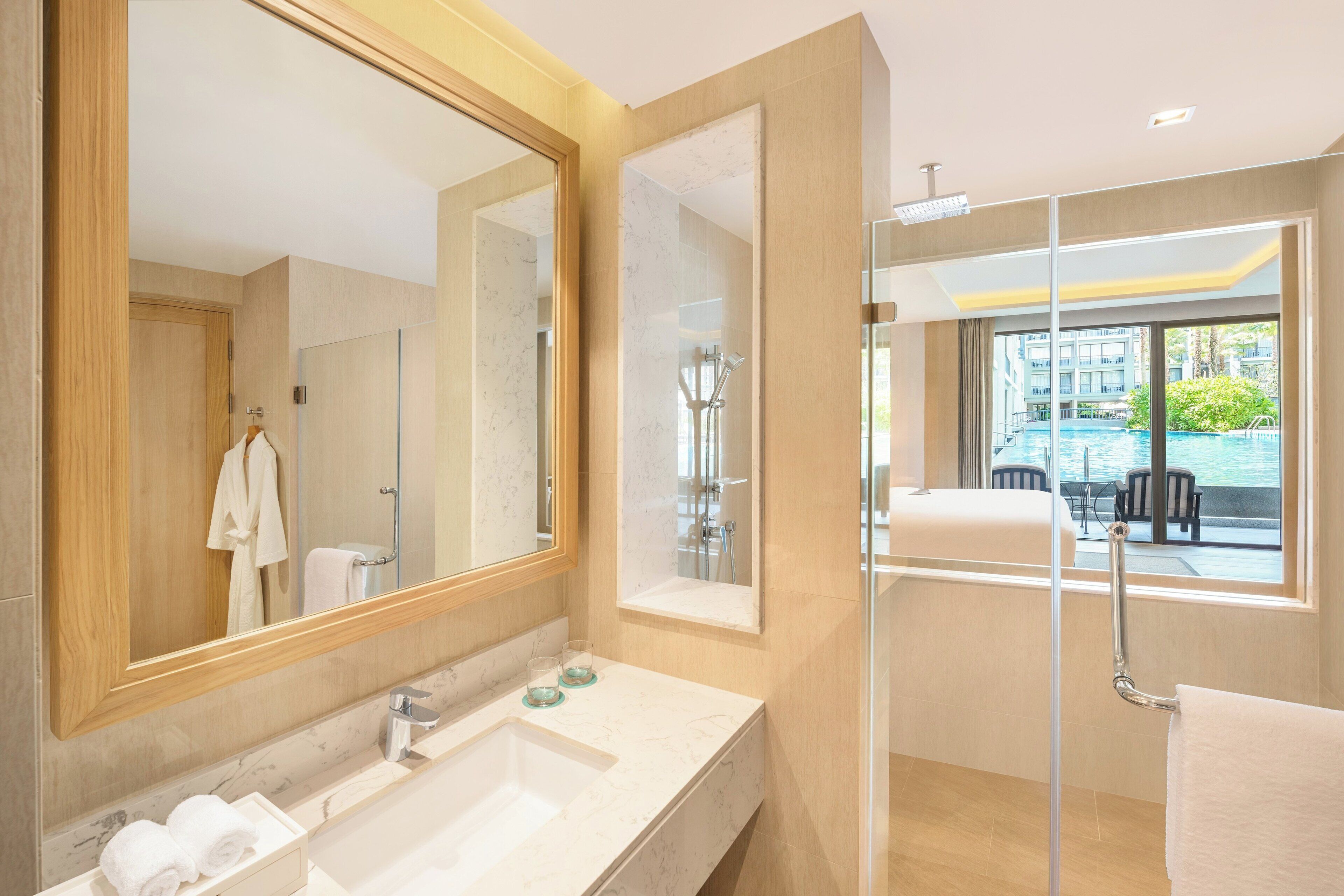 Un baño moderno con un espejo grande, cabina de ducha de vidrio y vistas a una piscina exterior.