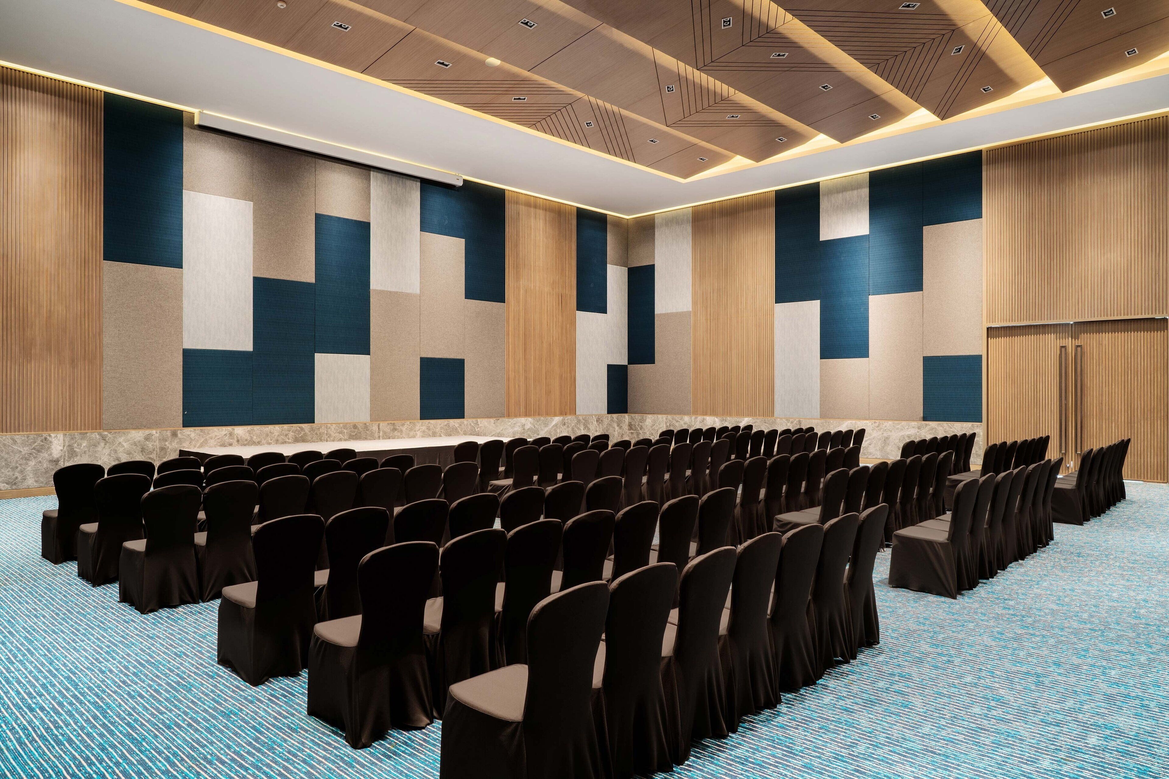 A conference room with rows of chairs, a long table, and a patterned carpet.