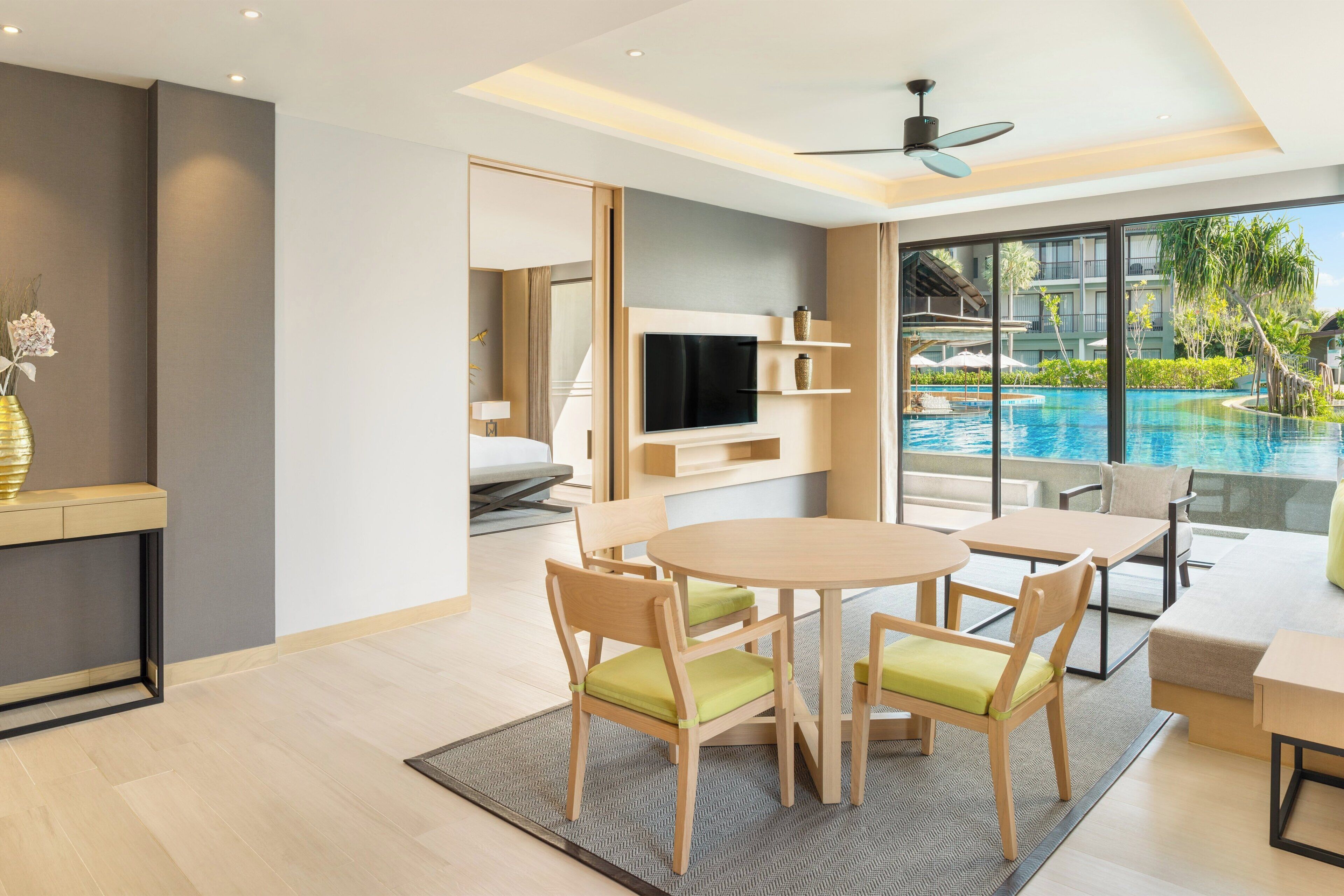 A modern hotel room with a pool view, a dining area, and a TV mounted on the wall.