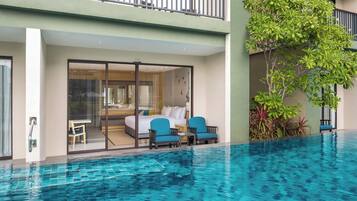 A modern hotel room with a glass door leading to a balcony, a poolside seating area, and a lush green plant.