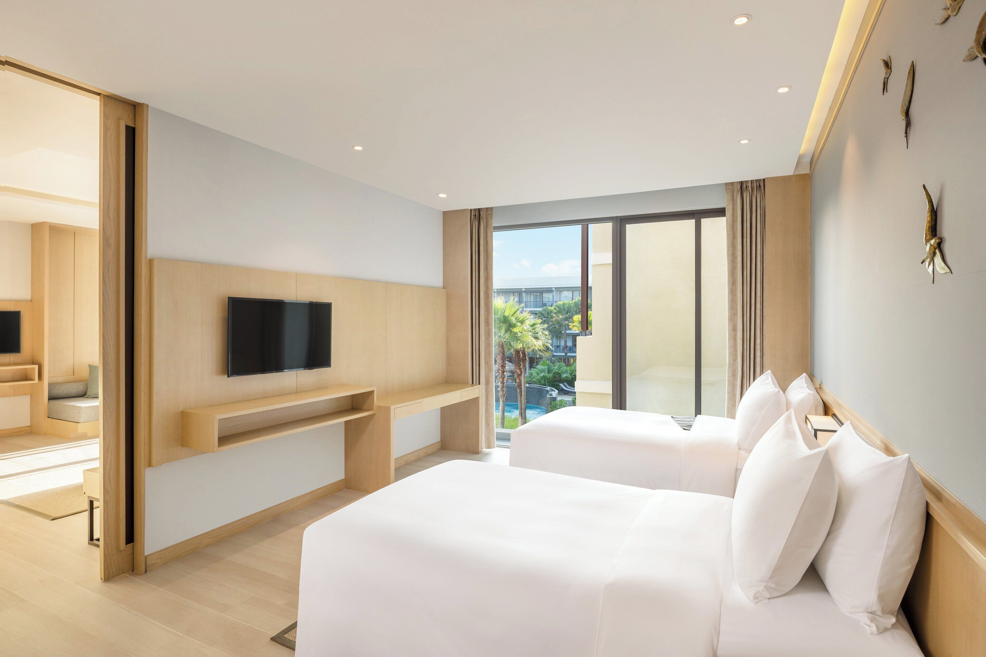 Ein Hotelzimmer mit einem großen Bett, einem an der Wand befestigten Fernseher und einem Balkon mit Blick auf die Stadt.