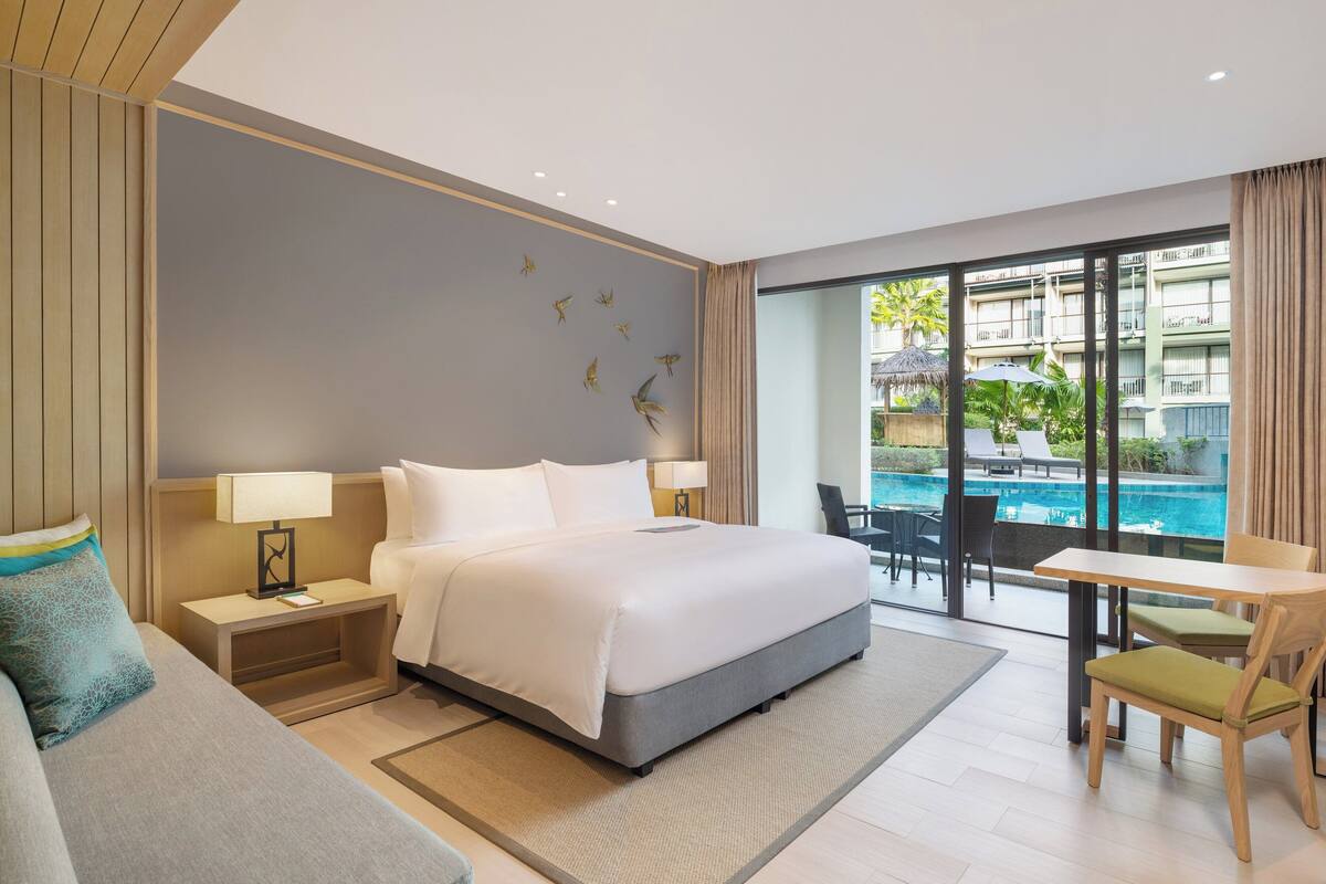 Een moderne hotelkamer met een groot bed, een bureau en uitzicht op een zwembad.