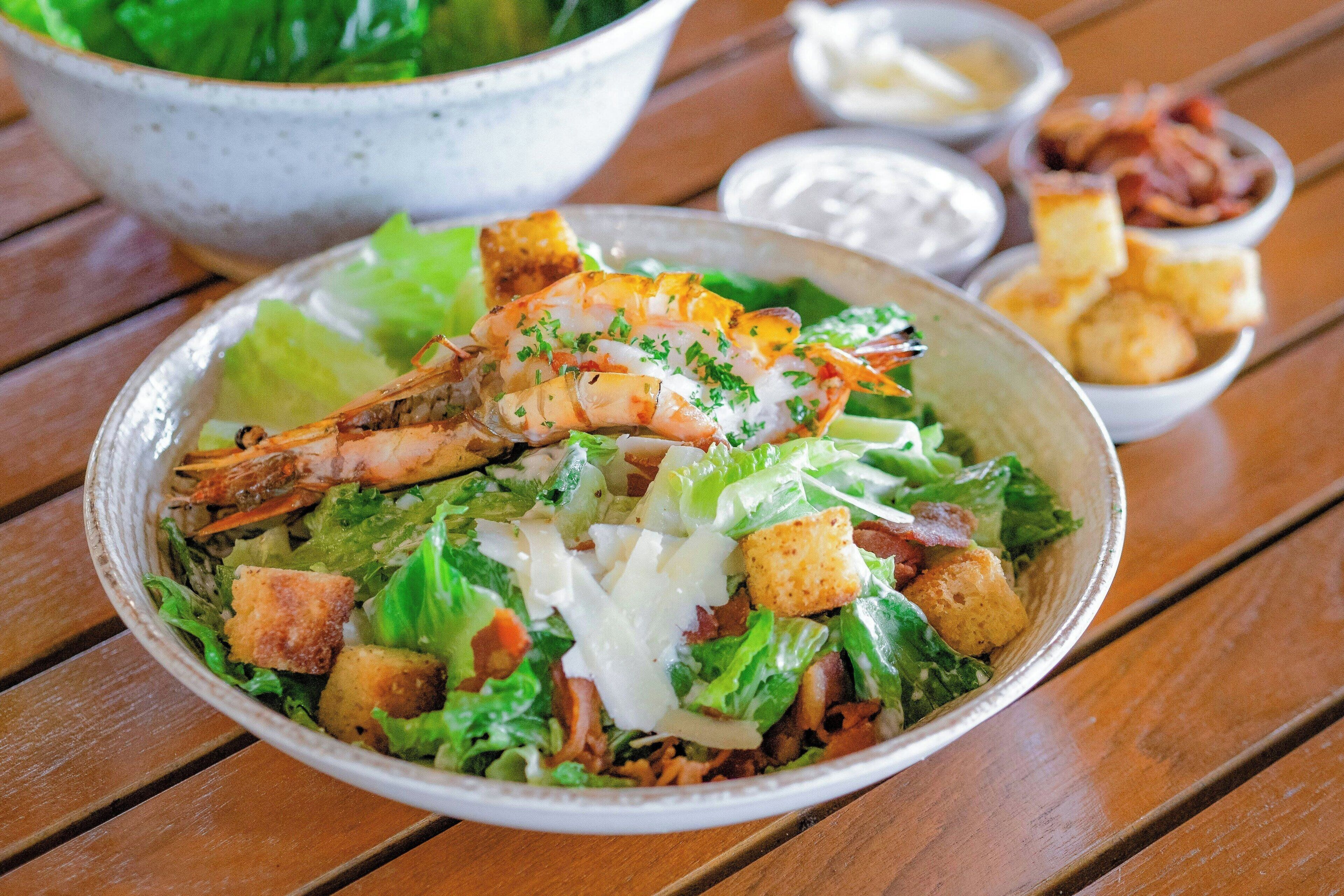 Ensalada de camarones con crutones y lechuga sobre una mesa de madera.