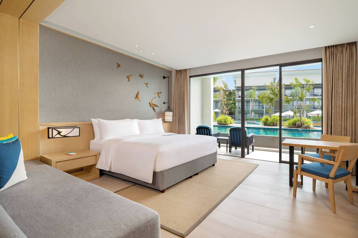Een moderne hotelkamer met een groot bed, een klein tafeltje en uitzicht op een zwembad.