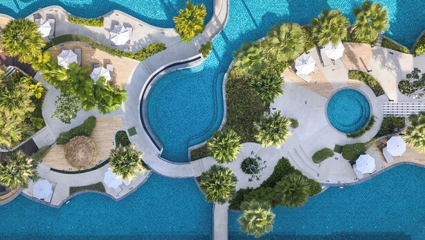Vue aérienne d’un complexe hôtelier doté de plusieurs piscines, de palmiers et d’espaces de détente.
