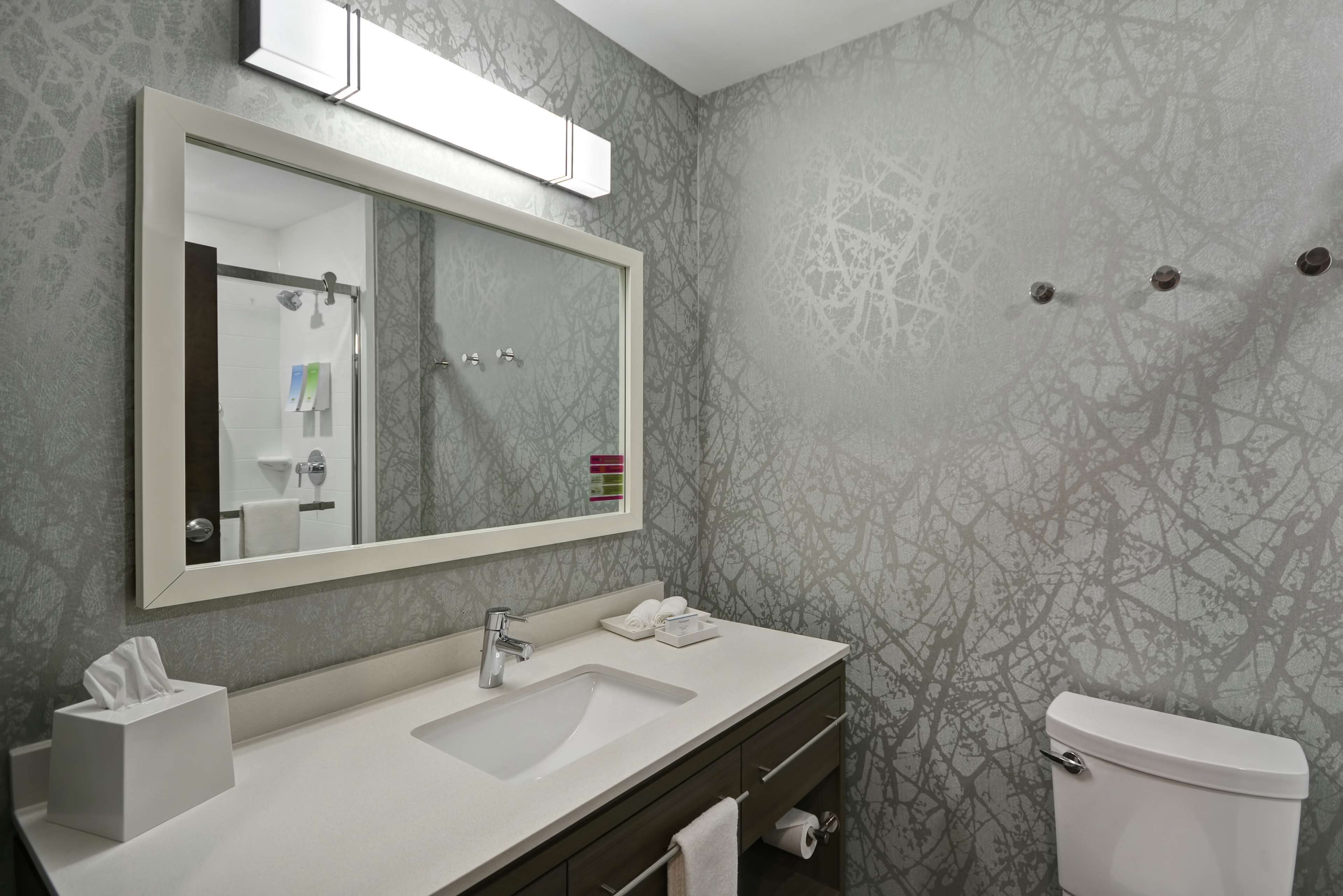 A bathroom with a large mirror, a sink, a toilet, and a towel rack.