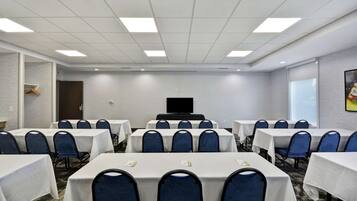 A conference room with tables and chairs, a television screen, and a door.