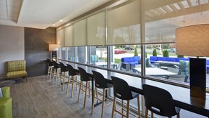 Un espace de détente intérieur moderne, doté d’une longue table et de chaises, ainsi que de grandes fenêtres offrant une vue sur l’extérieur.