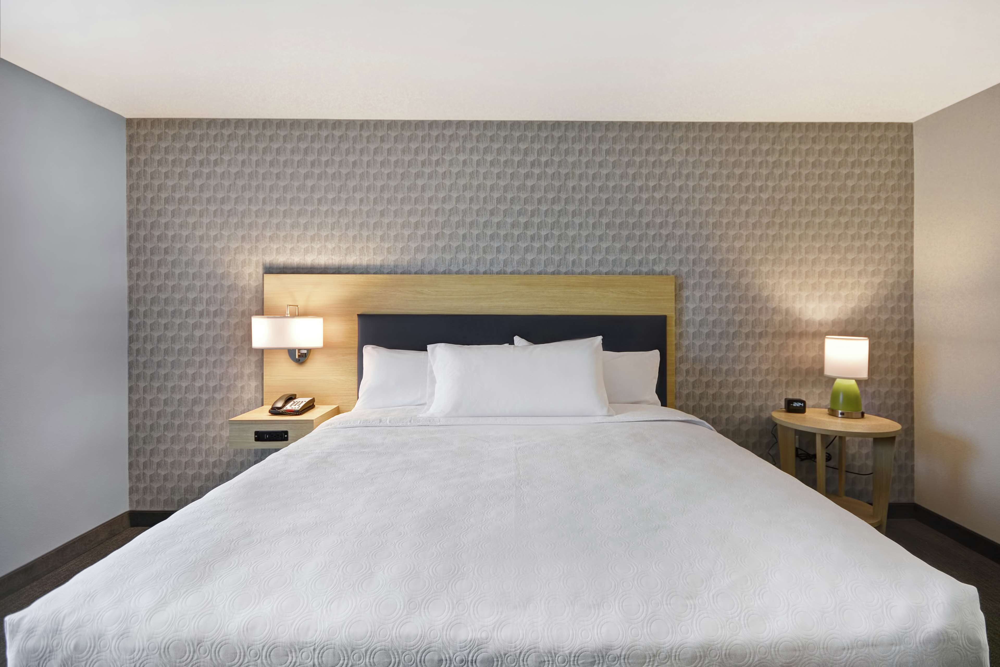 Ein Hotelzimmer mit einem großen Bett, zwei Nachttischen, einem Beistelltisch und einem Kopfteil.