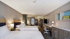 Une chambre d’hôtel avec deux lits, un bureau, une chaise, une télévision et une salle de bain visible à travers une porte ouverte.