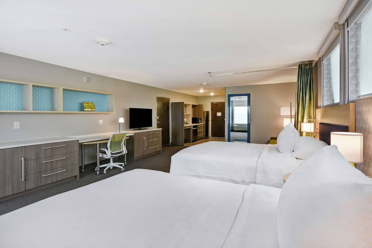 Une chambre d’hôtel avec deux lits, un bureau, une chaise, une télévision et une salle de bain visible à travers une porte ouverte.