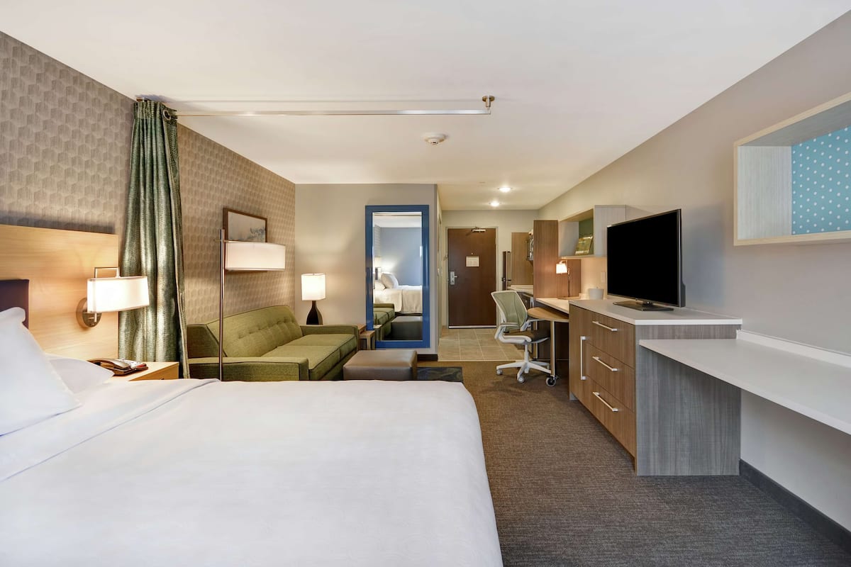 Une chambre d’hôtel avec un lit, un bureau, une chaise, une télévision et une salle de bain visible à travers une porte ouverte.
