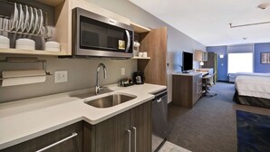 Une chambre d’hôtel de taille réduite, équipée d’une kitchenette, d’un lit, d’un bureau et d’une télévision.
