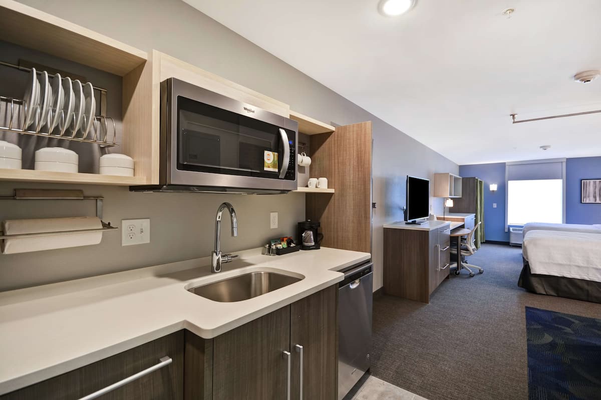 Une chambre d’hôtel de taille réduite, équipée d’une kitchenette, d’un lit, d’un bureau et d’une télévision.