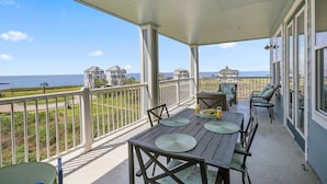 A covered balcony with a table set for dining, chairs, and a view of the ocean and neighboring houses. - Time Away Book 5+ nights & get 15% discount-Near Lazy River-3BD/2BA. Sleeps 9 (Galveston)