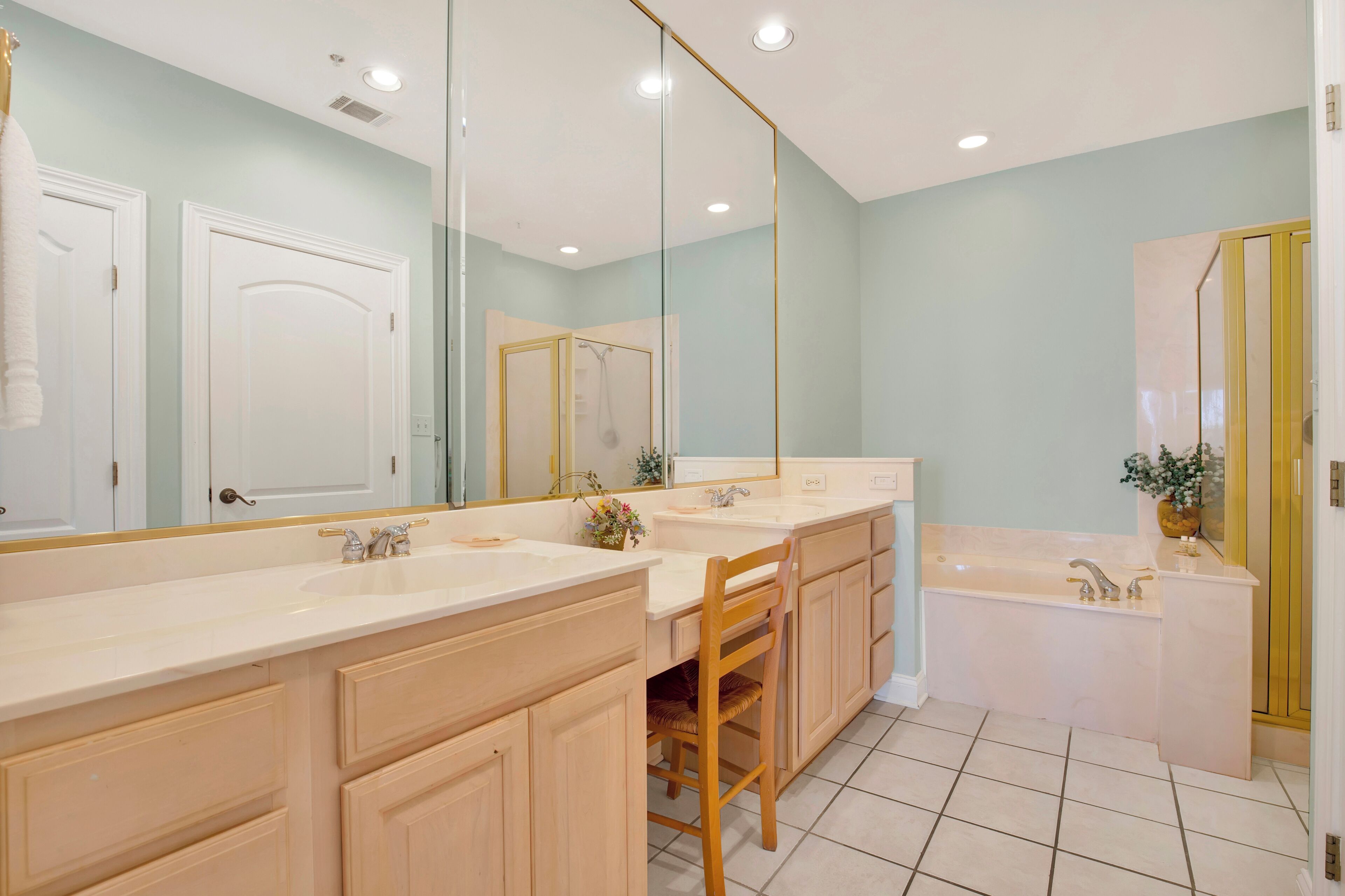 A bathroom with a large mirror, two sinks, a bathtub, and wooden cabinets.