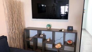 A living room with a dark sofa, a wooden console table with decorative shells, and a mounted flat-screen TV.