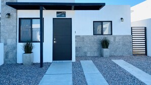 A modern building with a black door, a sign reading "Moana 11", and two potted plants.