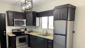 A modern kitchen with dark cabinetry, stainless steel appliances, a granite countertop, and a window with blinds.