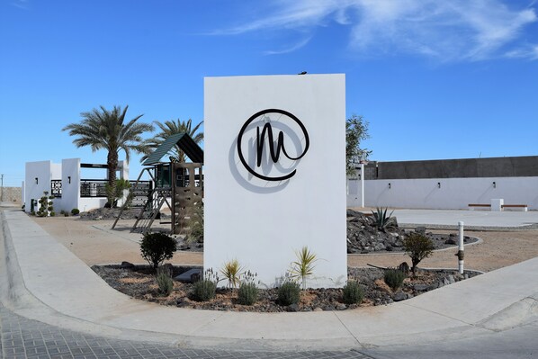A modern building with a prominent logo, a landscaped area with small plants, and a clear blue sky.