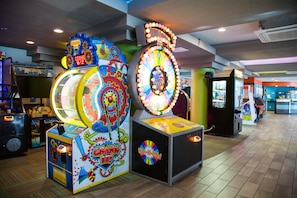 Een helder verlichte speelhal met diverse spelautomaten, waaronder een radspel en een grijpmachine.