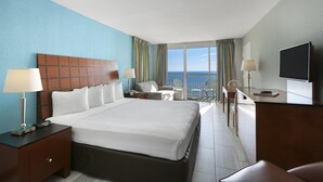 A hotel room with a large bed, a desk, a chair, a TV, and a view of the ocean. - Oceanfront King Efficiency w/ Balcony + Official On-Site Rental Privileges (Myrtle Beach)