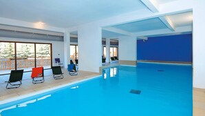 An indoor swimming pool with clear blue water, surrounded by white walls and a wooden deck. - Studio Cosy au Pied des Pistes avec Accès Piscine (Vars)
