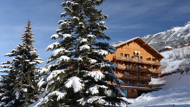 A wooden chalet with balconies, surrounded by snow-covered trees and mountains. - Studio Cosy au Pied des Pistes avec Accès Piscine (Vars)