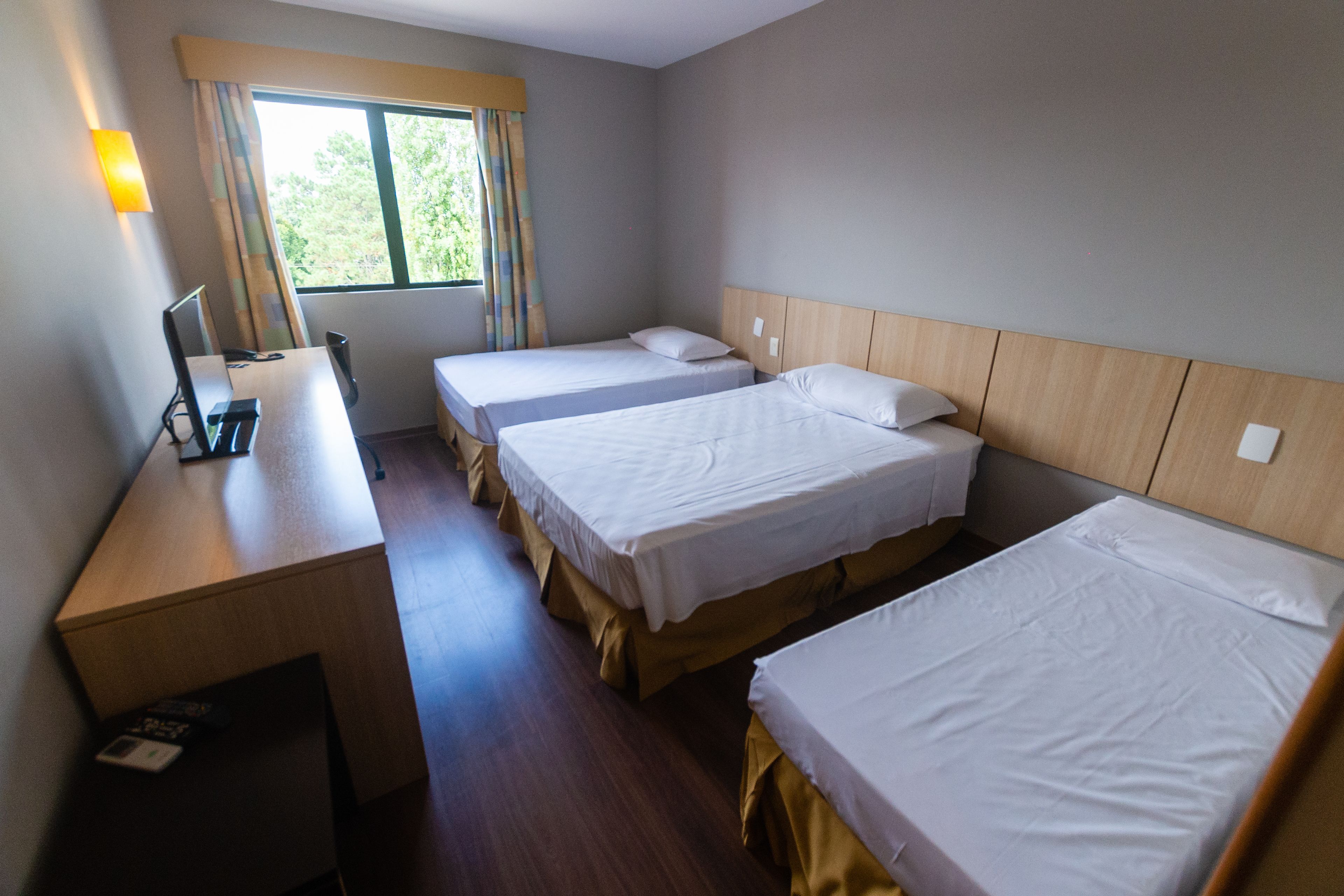 A hotel room with two single beds, a desk with a chair, a lamp, and a window with curtains.