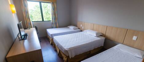 A hotel room with two single beds, a desk with a chair, a lamp, and a window with curtains.