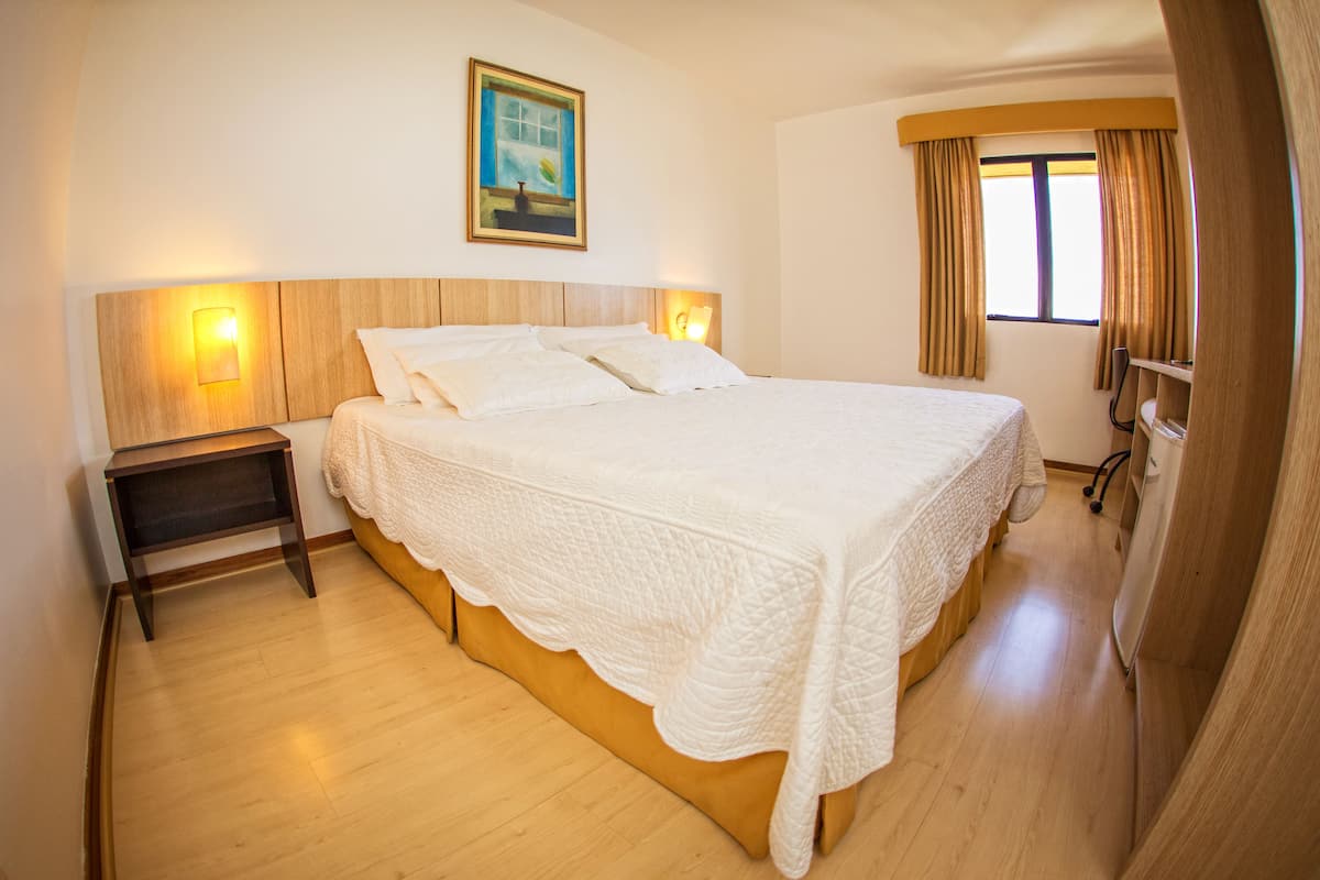 A neatly made bed with a quilted blanket, a bedside table with a lamp, and a painting on the wall.