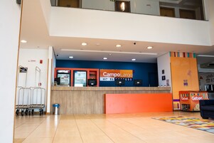 Zona de recepción de un hotel con una decoración en tonos azul y naranja, una máquina de helados Geben y un carrito de equipaje.
