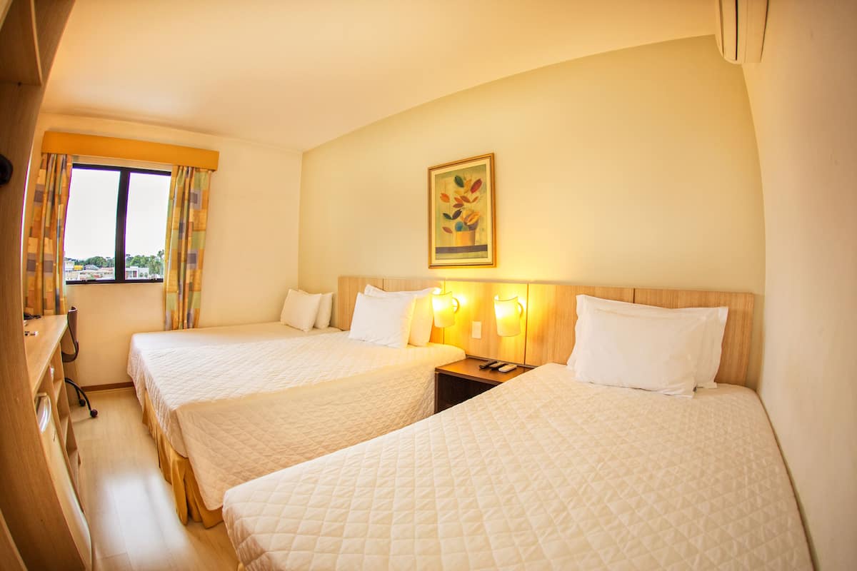 A hotel room with two beds, a desk, a chair, a window with curtains, and a painting on the wall.