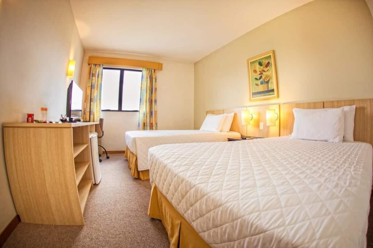 A hotel room with two beds, a desk, and a chair.