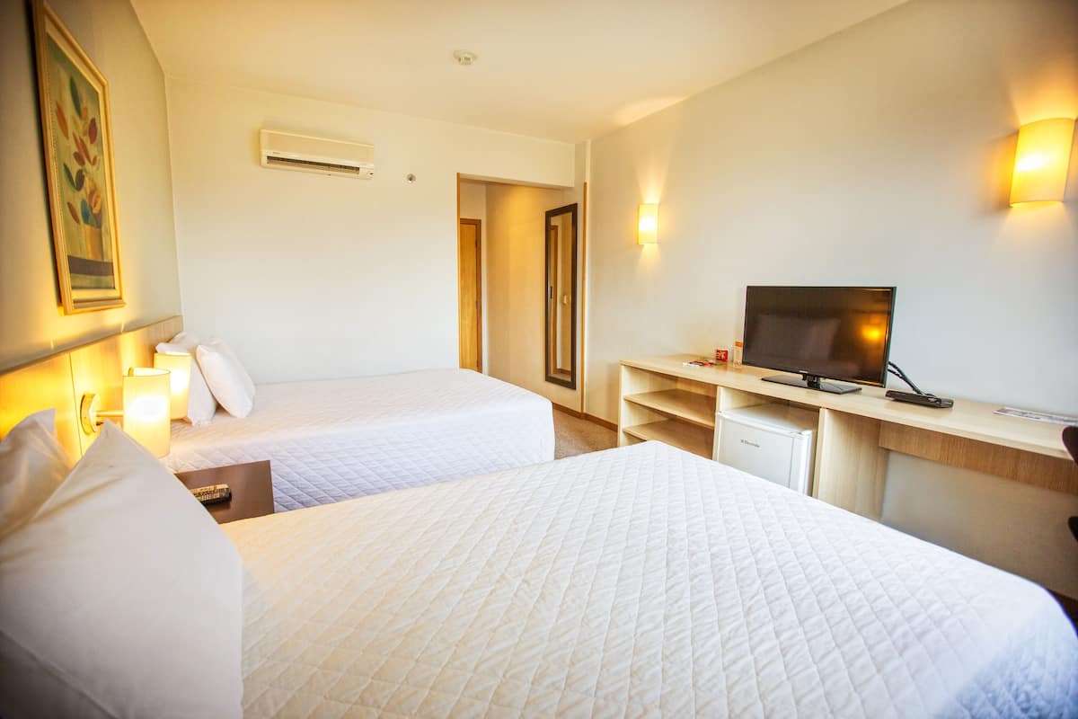 A hotel room with two beds, a desk with a television, and a small refrigerator.