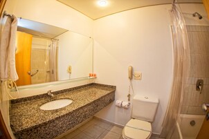 Un baño con lavamanos de granito, un espejo, inodoro y zona de ducha.