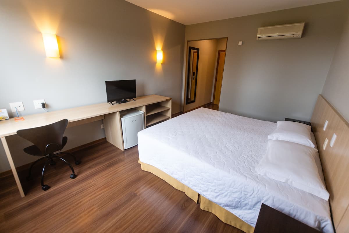 A hotel room with a bed, a desk with a computer, a chair, and a TV.