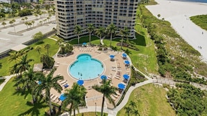 A high-rise hotel with a pool area, palm trees, and a beach view.
