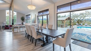 Un comedor amplio con una mesa grande y sillas, un candelabro y vistas a una piscina y zona de estar exterior.