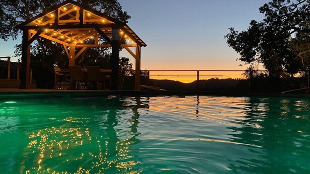 Una piscina con un pabellón de madera al atardecer.