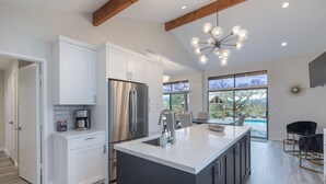 Una cocina moderna con armarios blancos, un refrigerador de acero inoxidable y una isla grande. Hay un comedor con vista a la piscina.