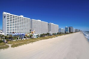 A beachfront hotel with multiple high-rise buildings, a sandy beach, and a clear blue sky. - Oceanfront Suite at Family Friendly Resort + Official On-Site Rental Privileges (Myrtle Beach)