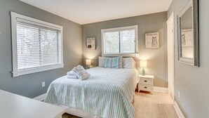 Quarto com cama, duas mesas de cabeceira, um criado-mudo e duas janelas com persianas.