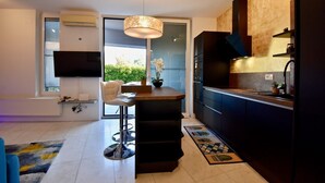 A modern kitchen with a central island, a dining area with a white chair, and a TV mounted on the wall. - Amazing luxury apartment 200 m from the beach (Pula)