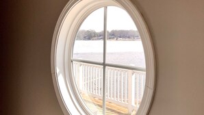 A round window with a view of a wooden deck and a body of water. - PONTOON BOAT NOW INCLUDED! 7 BEDS, HOT TUB Updated Lakefront Cottage - Book Now (Norton Shores)