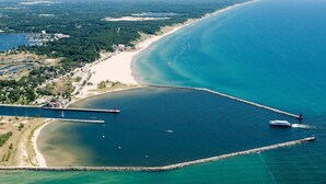 An aerial view of a coastal area with a beach, a pier, and a lighthouse. - PONTOON BOAT NOW INCLUDED! 7 BEDS, HOT TUB Updated Lakefront Cottage - Book Now (Norton Shores)